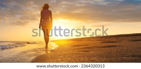 Photo of a young stunning woman walking along the seashore. Fresh sea breeze, a girl watches the sunset and walks towards the sun's rays