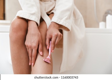 Photo of young woman in bathroom shaving her legs.