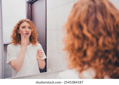 Photo of young woman brushing teeth suffering pain toothache looking in mirror in bathroom morning indoors - Powered by Shutterstock