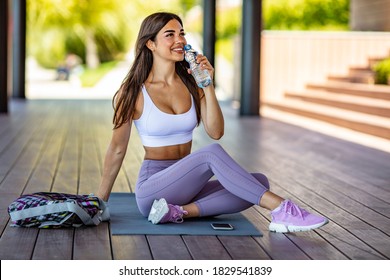 Photo of young Woman drinking water from bottle. Caucasian female drinking water after exercises or sport. Beautiful fitness athlete woman drinking water after work out exercising on sunset evening