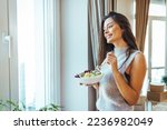 Photo of young woman enjoying a delicious salad at home during the day. Portrait of a young and cheerful woman eating healthy salad. Healthy eating, wellbeing and lifestyle concept