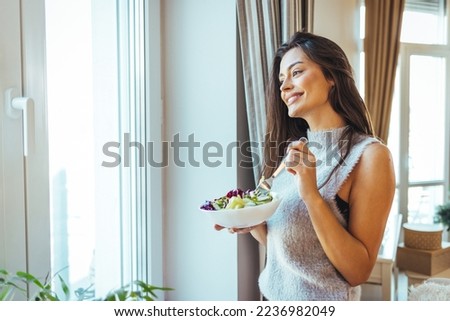 Photo of young woman enjoying a delicious salad at home during the day. Portrait of a young and cheerful woman eating healthy salad. Healthy eating, wellbeing and lifestyle concept