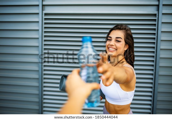 Photo of Young woman hand giving or serving a\
bottle of fresh cold drinking water to a woman after fitness\
exercise. Friend giving water bottle after exercising outdoor\
together. Sharing water\
outdoor
