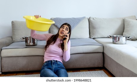 Photo of a young woman holding yellow bucket while water droplets leak from ceiling. Roof leaking. Unhappy woman looks at the ceiling while collecting water at home during the day.  - Powered by Shutterstock