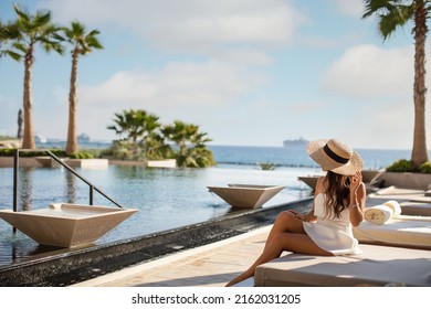 Photo of a young woman sitting near pool and enjoying the view. Luxury resort 