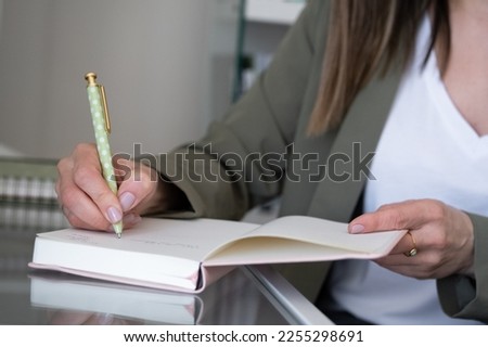 PHOTO OF A YOUNG WOMAN'S HANDS TAKING NOTES IN A NOTEBOOK IN THE OFFICE