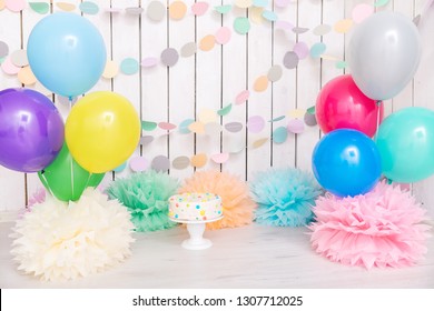 Photo zone with paper garlands, balloons, paper balls, pom poms, confetti and cream cake. Birthday cake. Smash cake. One year. Pink, white, blue, green, yellow colors. Rainbow