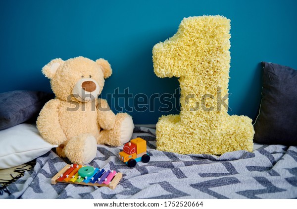Photo zone with paper garlands, paper flowers,\
pillows, bear and number one on floor against blue background, copy\
space. Birthday concept. One\
year.