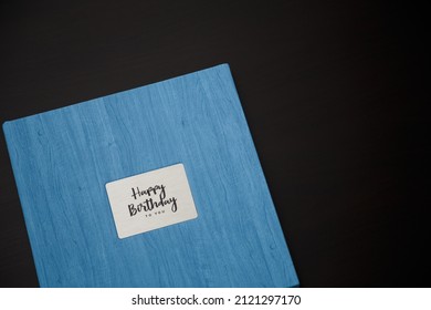 Photobook, photoalbum in blue leather cover on black table background with metallic shield and inscription Happy Birthday to you. Top view, copy space.