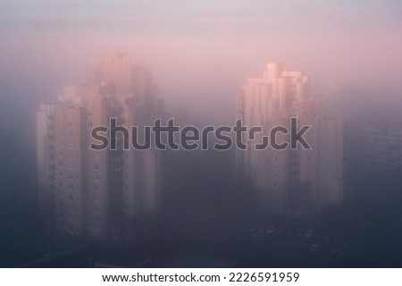 Photograph of apartment buildings in the suburbs of Paris in the fog on a winter morning with a sunrise that tints the fog pink and blue.