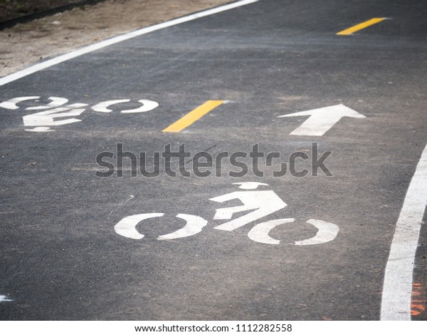 Photograph of a brand new asphalt bike\
path in Chicago with two way traffic bike symbols and arrows\
painted in white warning pedestrians of passing\
bicycles.