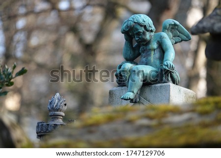 photograph of a bronze sculpture (statue) of a child angel in Père Lachaise cemetery (in Paris). The angel is holding his head with one hand.