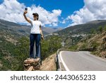 photograph of a brunette Latina girl, perched on a pole while taking a photo (selfie), with a town in the mountains in the background; in the Alpujarra, Granada