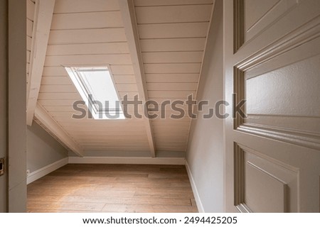 The photograph captures an empty attic room featuring a slanted roof and a small skylight window, creating a bright and cozy atmosphere ideal for various renovation ideas.