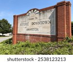 The photograph captures the welcoming sign for the city of Anniston, Alabama, standing proudly against a vibrant blue sky. 