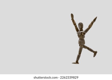 Photograph of a dark colored wooden mannequin with light gray background, it is in motion, with arms open and stretched upwards. Photo to be able to cut out. Concepts. Selective focus. Space for copy