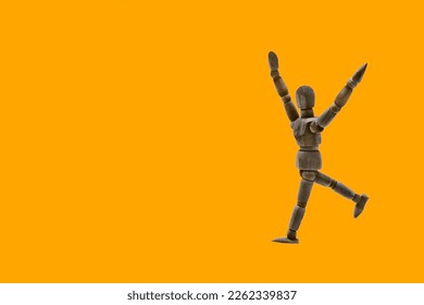 Photograph of a dark colored wooden mannequin with orange background, it is in motion, with arms open and stretched upwards. Photo to be able to cut out. Concepts. Selective focus. Space for copy