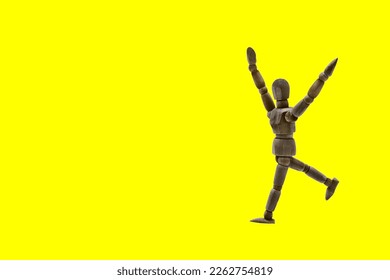 Photograph of a dark colored wooden mannequin with yellowed background, it is in motion, with arms open and stretched upwards. Photo to be able to cut out. Concepts. Selective focus. Space for copy