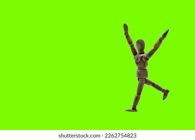 Photograph of a dark colored wooden mannequin with light green background, it is in motion, with arms open and stretched upwards. Photo to be able to cut out. Concepts. Selective focus. Space for copy