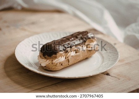 A photograph of a delectable eclair resting on a pristine white ceramic plate