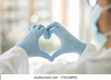 
Photograph of a doctor made with his back to him who is creating a heart with his hands in which he wears gloves, we also intuit that he has a sanitary mask on his face