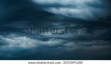 Photograph of a dramatic isolated Asperitas cumulus thunderstorm cloud as it swirls and moves across the sky bringing rain with dark blue textures and undulating ripples and waves of light.