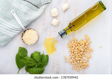 Photograph of fresh basil pesto ingredients including virgin olive oil, pine nuts, garlic, basil and Parmesan-Reggiano cheese with a kitchen towel on the counter