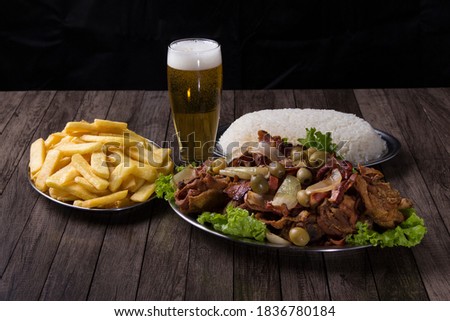 Photograph of fried chicken with rustic onions and bacon, accompanied by a refreshing glass of beer with foam, French fries and white rice. Horizontal gourmet photography.