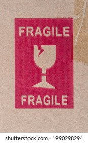 Photograph Of A Generic Red FRAGILE Postage Stamp On A Brown Cardboard Box Shot Straight On.