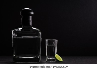 Photograph of a glass bottle on a black background, accompanied by a tequila shot glass with a lemon wedge - Powered by Shutterstock