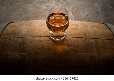 A photograph of a glass of whiskey sitting atop of a whiskey barrel. From above you can see the amber aromas from the whiskey and the groves and slits of the American white oak.