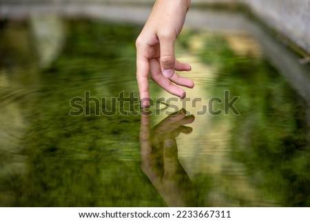 Photograph of a hand about to touch the water and seeing its reflection