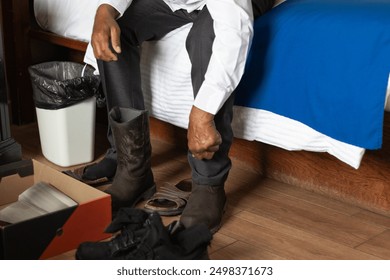 Photograph of the hands of an older man who is formally dressed, sitting on the bed in a hotel room, putting on boots, in preparation for work - Powered by Shutterstock