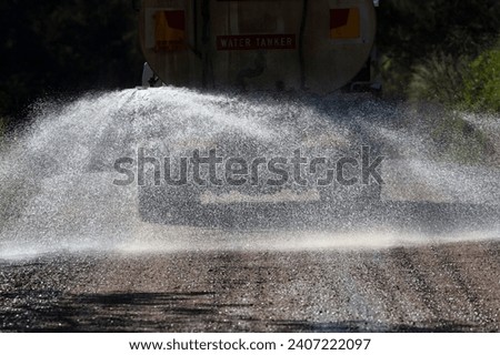 Photograph of a large water tanker spraying water on a dirt road that is under repair running through a forest to reduce dust in the Blue Mountains in regional Australia