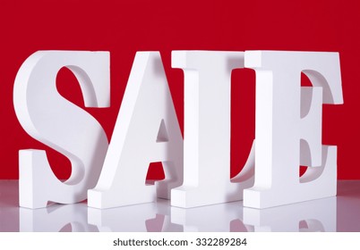 Photograph of Large white Sale letters made out of wood on reflective glass table with red background for retail shopping sales concept. 