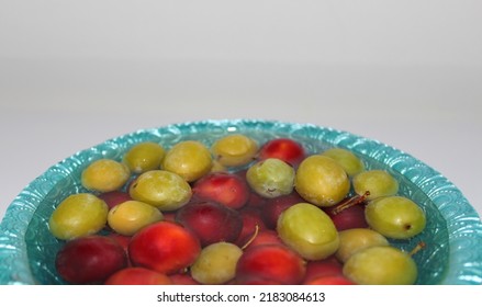 Photograph of luscious red plums and green plums on a white table, in water on a blue plate, fruits in water - Shutterstock ID 2183084613
