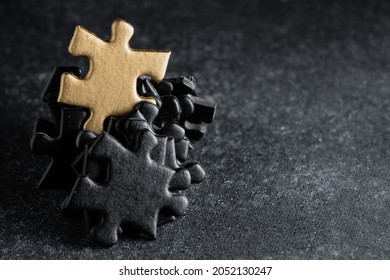 Photograph Of Many Black Puzzle Pieces Where A Gold Piece Is Also Shown In The Center. Standout Concept. Unique, Leader, Different.