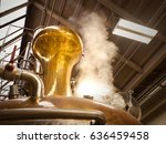 A photograph of a pot still in a whiskey distillery. Steam is rising from the still to the top of warehouse as the still is going through a distillation process.