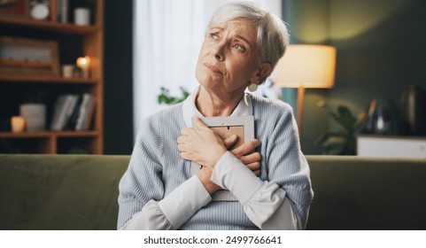 Photograph, sad and thinking with senior woman on sofa in living room of retirement home for grief. Loss, memory and pain with unhappy elderly person in apartment for mourning, reflection or regret - Powered by Shutterstock