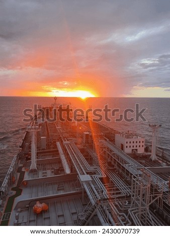 The photograph showcases a serene sunrise at sea, taken from a ship. The sea stretches out, calm and vast, under the painted skies, highlighting the solitude and majesty of the maritime world.
