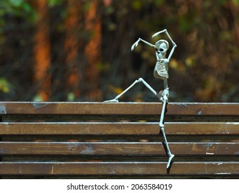 Photograph of a skeleton on the bench in the public park at night. Agressive skeleton toy. 
He scares passers-by. Natural dark background. Halloween concept.