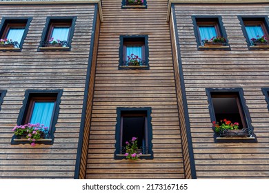 A Photograph Of A Symmetry Building Facade With Wooden Trim And Many Windows. Beautiful Red Geraniums In Pots Grow On The Windowsills.