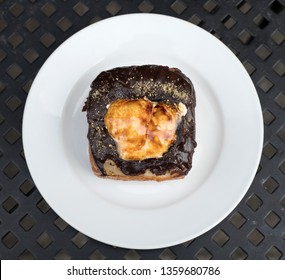 A Photograph Of A View From Above Of A Square Shaped Smores Flavored Doughnut With Burnt Marshmallow On Top, Placed On A White Plate.