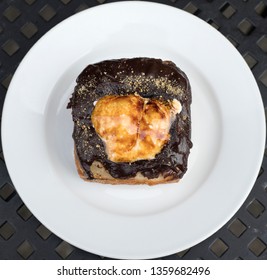 A Photograph Of A View From Above Of A Square Shaped Smores Flavored Doughnut With Burnt Marshmallow On Top, Placed On A White Plate; Cropped To Be 1x1.