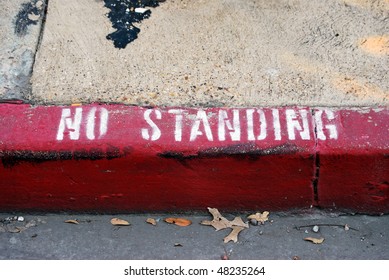 A Photograph Of The Words No Standing Painted On A City Sidewalk Curb.