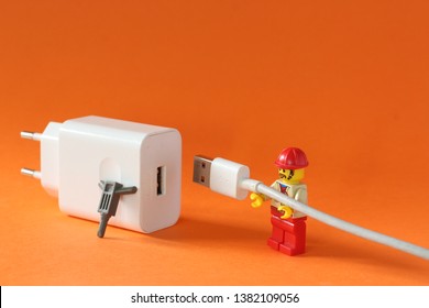 A photograph of working man fixing mobile phone charger isolated on orange background. Editorial close up image of Lego minifiure rapair tech items.