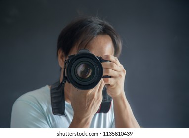 Photographer With Camera In Hand Looking Through The Camera Lens. Gray Background