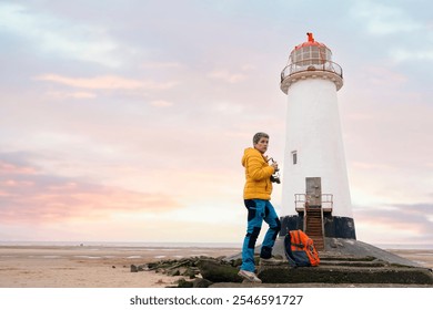 A photographer captures the beauty of a lighthouse at sunset by the beach, enjoying a tranquil moment in nature - Powered by Shutterstock