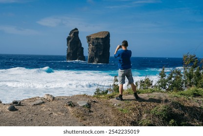 Photographer capturing the iconic rock formations emerging from the ocean waves under a clear blue sky, showcasing the dramatic coastal landscape and powerful beauty of nature. - Powered by Shutterstock