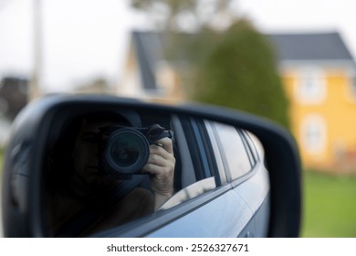 A photographer capturing a reflection through a car's side mirror, with a blurred background of a house and greenery. - Powered by Shutterstock